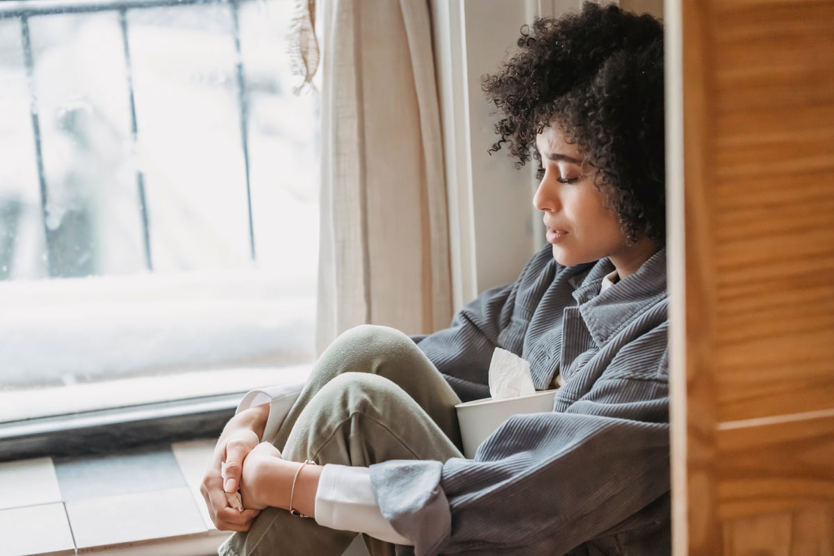 Desperate black woman embracing knees suffering from difficulties